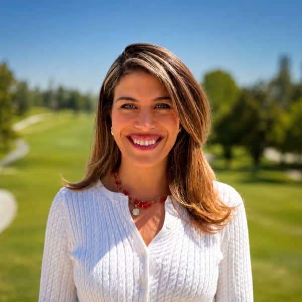 Smiling woman in white cardigan and red necklace on a golf course