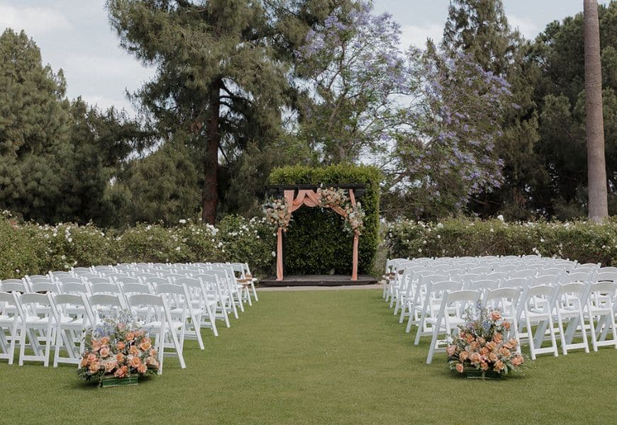 Lawn ceremony setup with white chairs and a floral-draped arbor at El Dorado