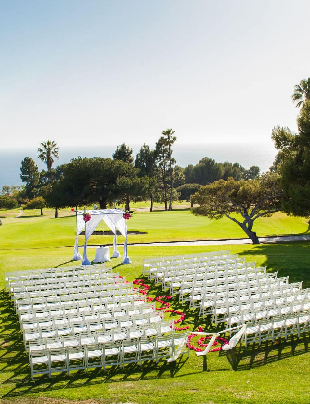 Draped ceremony canopy and white chairs on a clifftop lawn overlooking the ocean