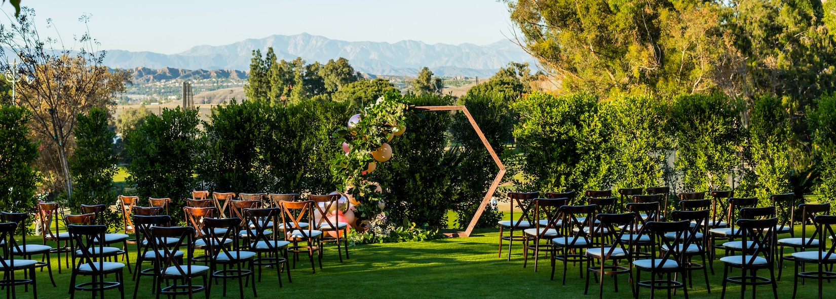 Outdoor ceremony lawn with wooden chairs facing a hexagonal floral arch