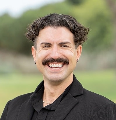 Greg Varley, smiling in a black blazer on a golf course