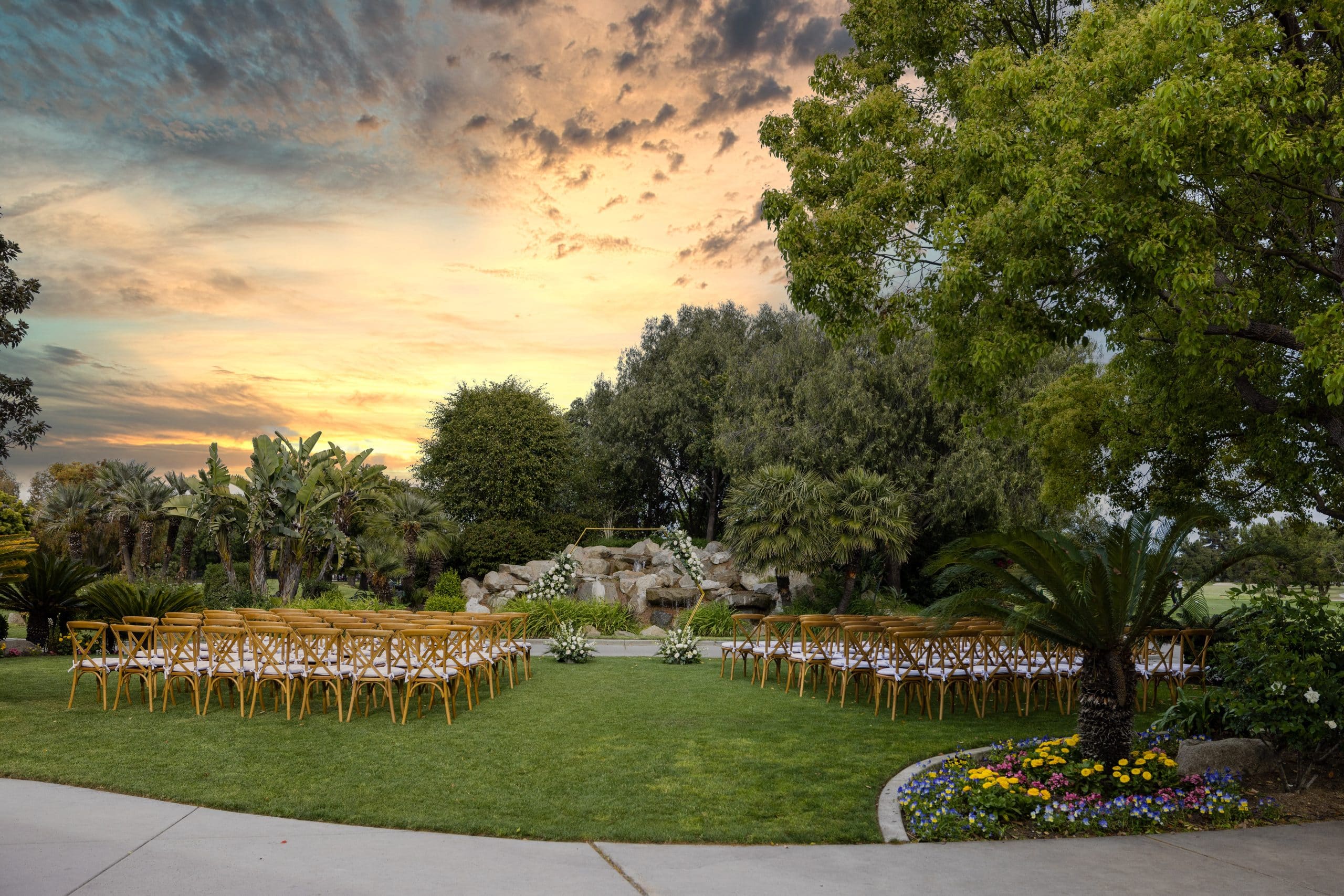 Garden ceremony lawn at sunset with wooden chairs facing a floral arch