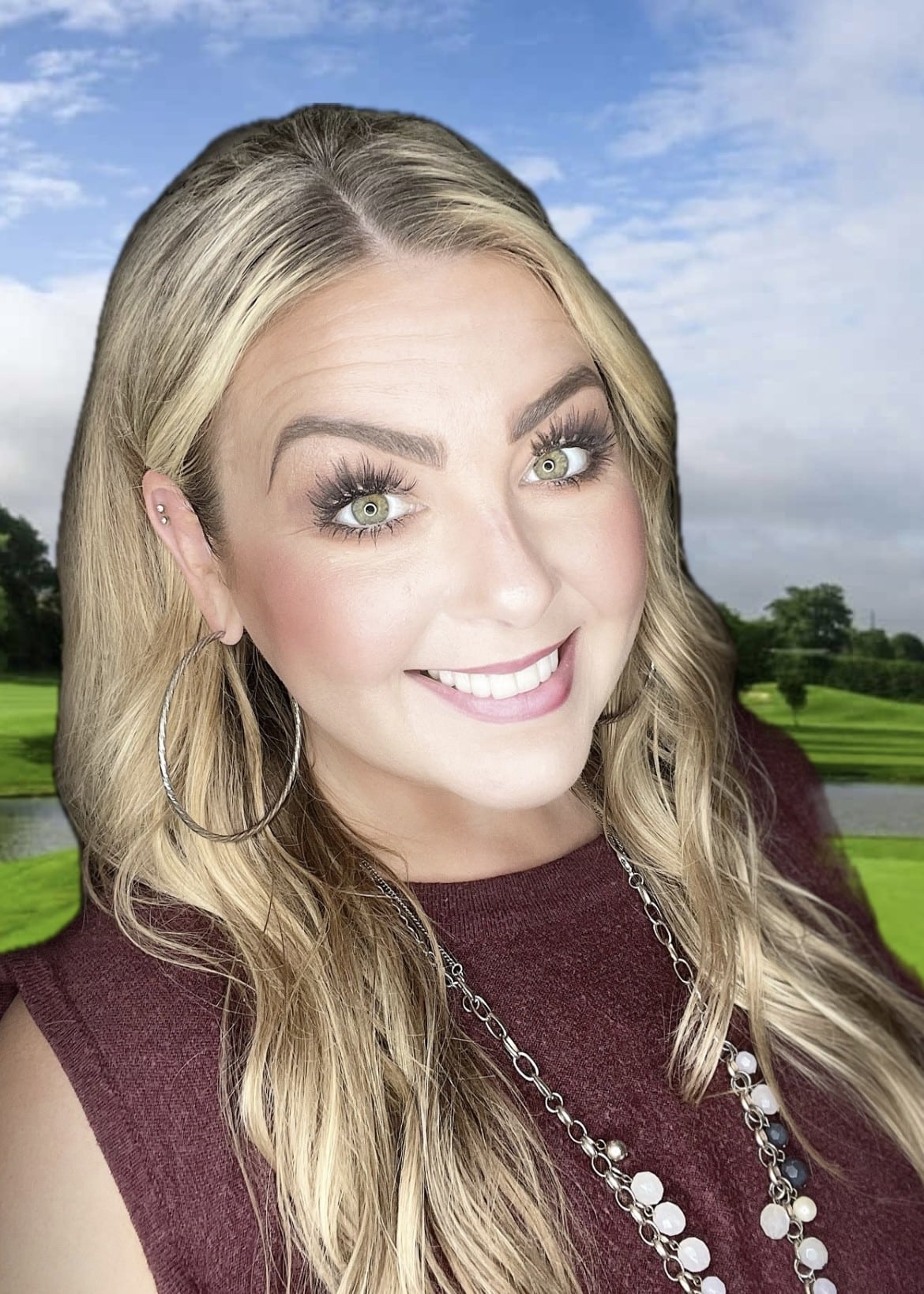 Smiling woman with blonde hair in a burgundy top on a golf course