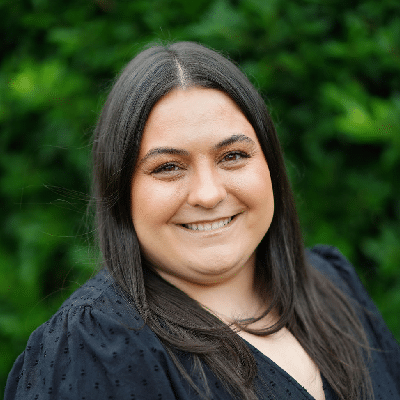 Alyssa, smiling in a black blouse against a green hedge