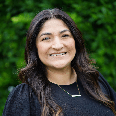 Gaby, smiling in a black top with a gold bar necklace