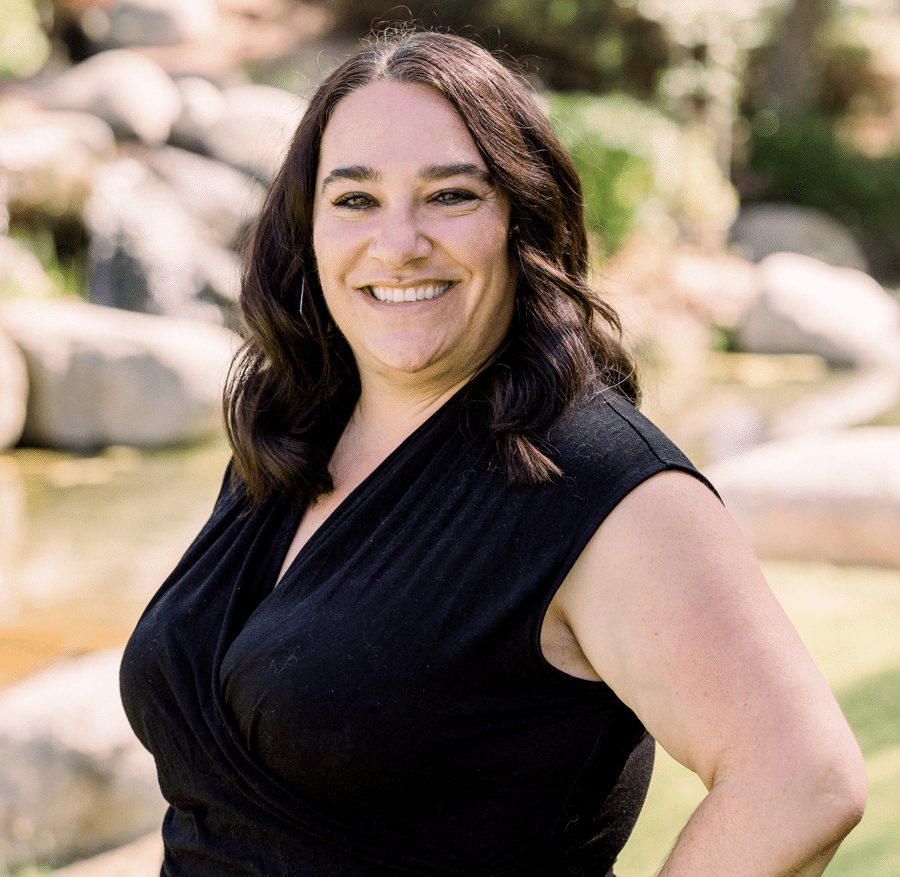 Selina, smiling in a black sleeveless top beside a rock water feature