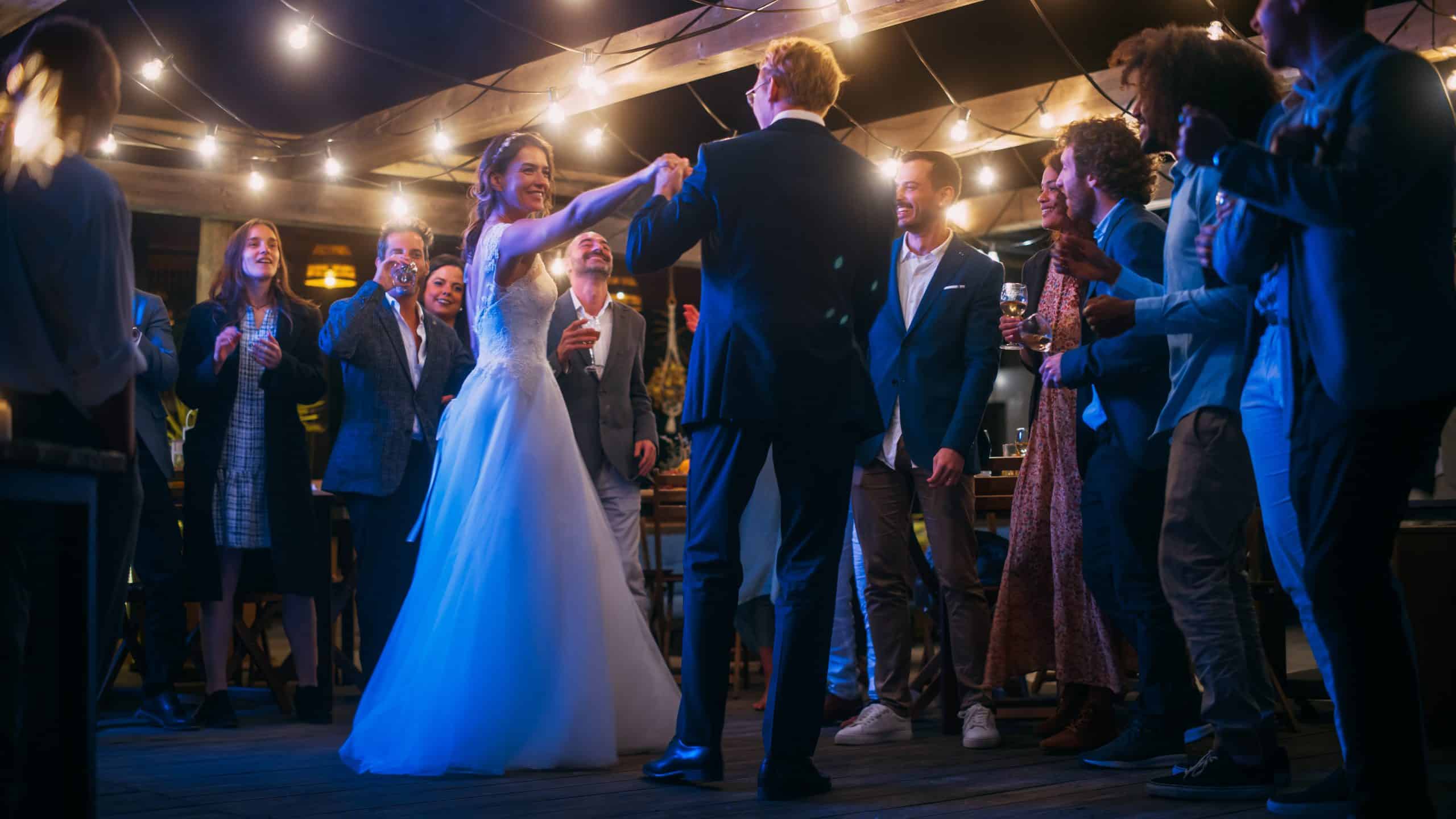 Bride and groom dancing under string lights as guests watch and applaud