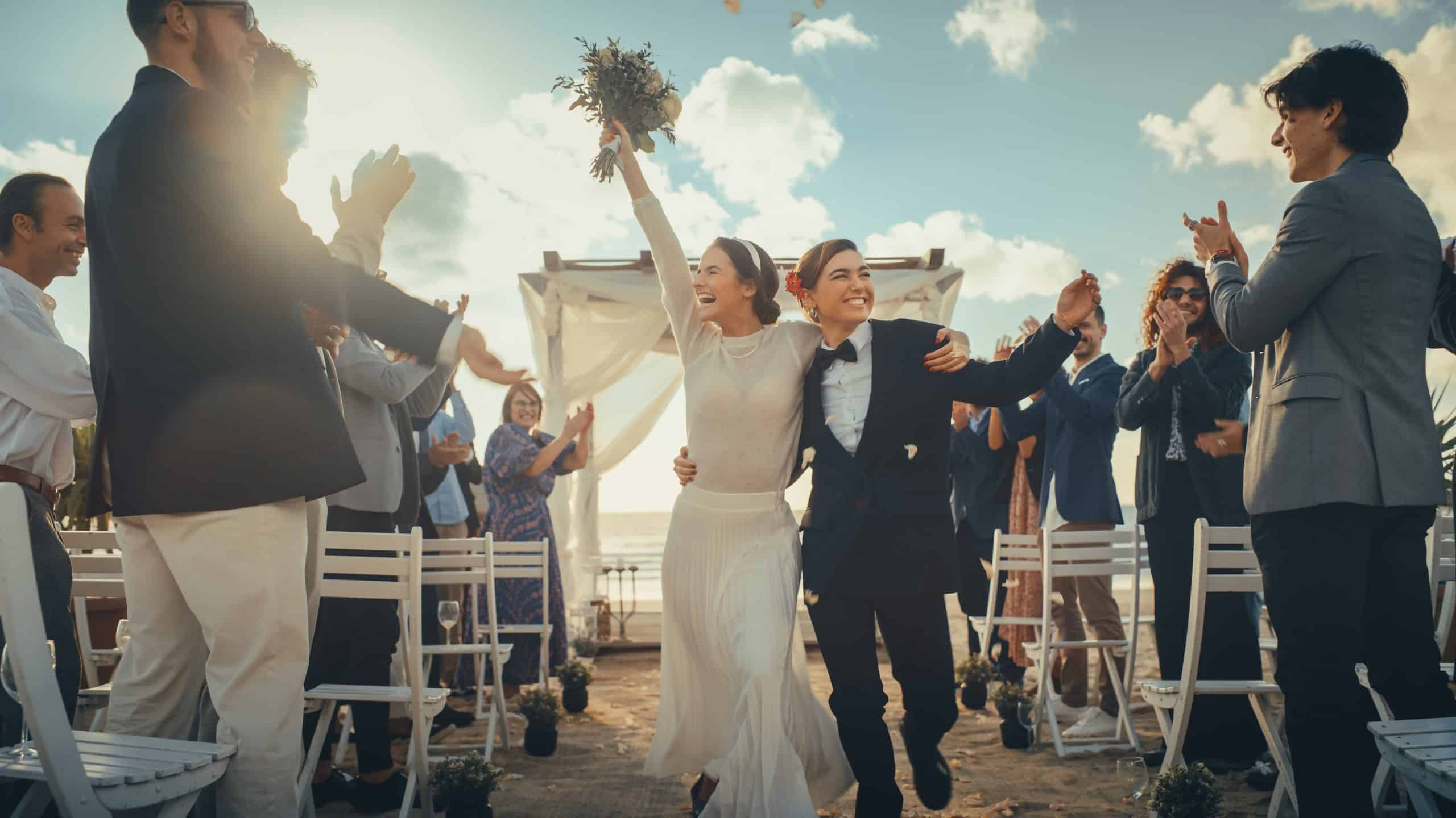 Newlywed couple walking up the aisle as guests applaud and toss petals