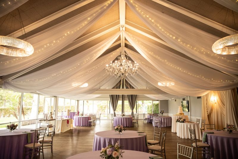 Indoor reception hall with white ceiling draping, chandelier and lavender-linen tables at Diamond Bar