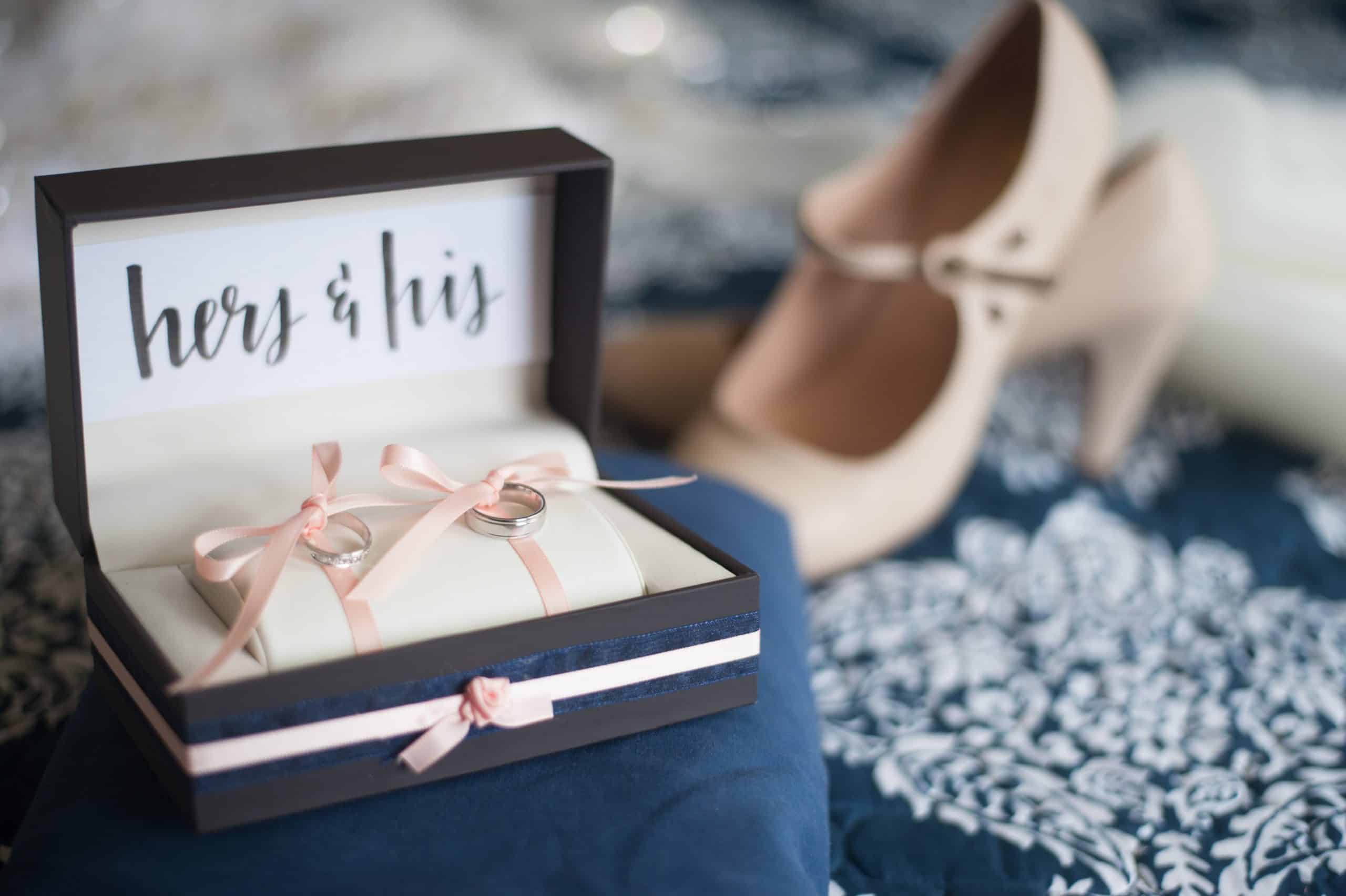 Wedding rings in a hers and his keepsake box beside blush bridal heels