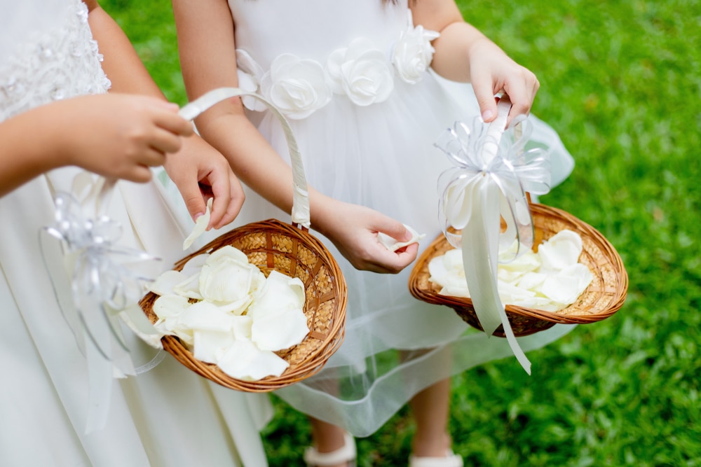 Two flower girls in white dresses holding baskets of ivory rose petals