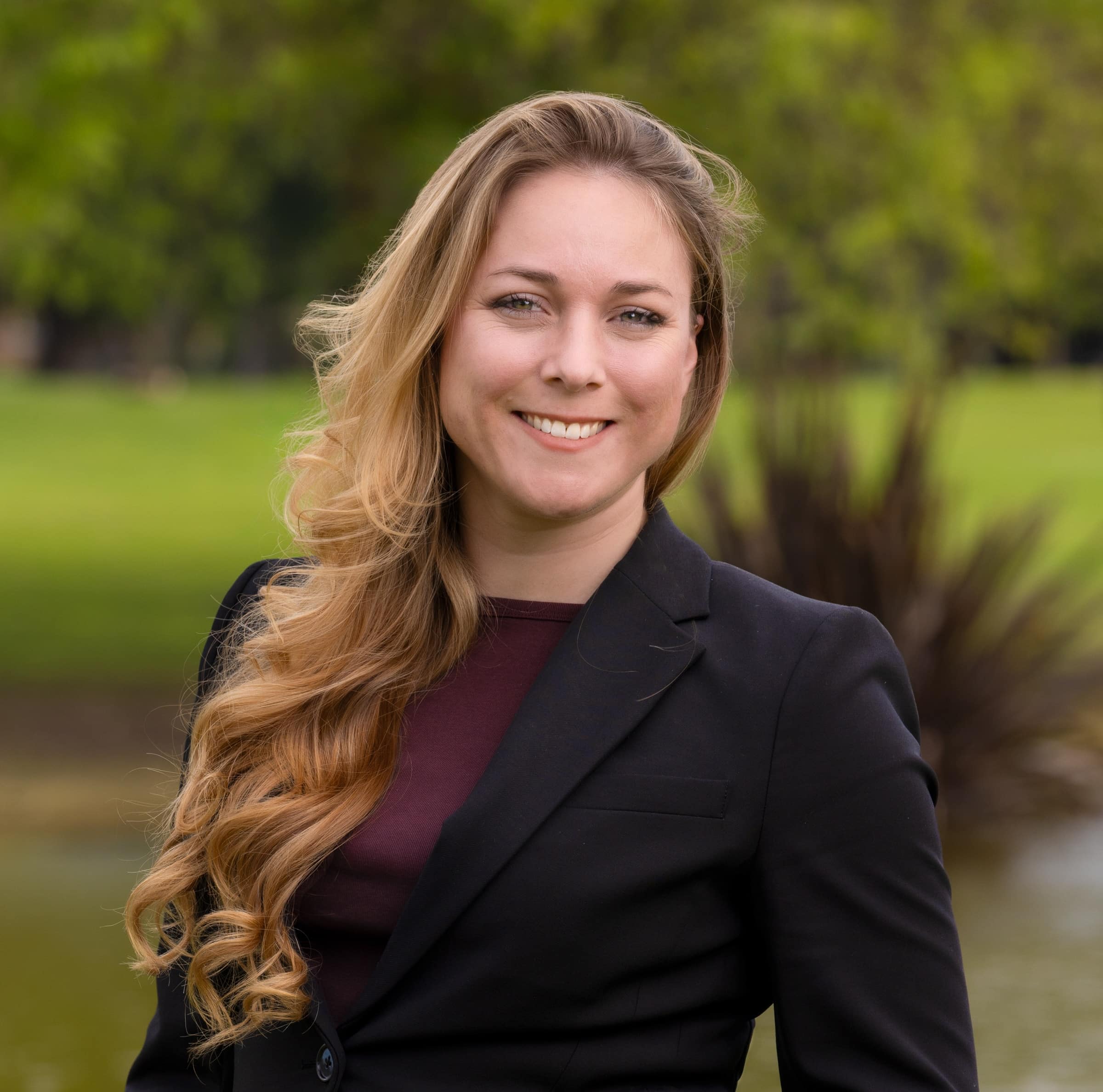 Ariel, smiling in a black blazer outdoors on the golf course