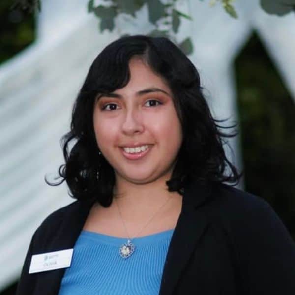Smiling woman in a black blazer and blue top wearing a staff name badge
