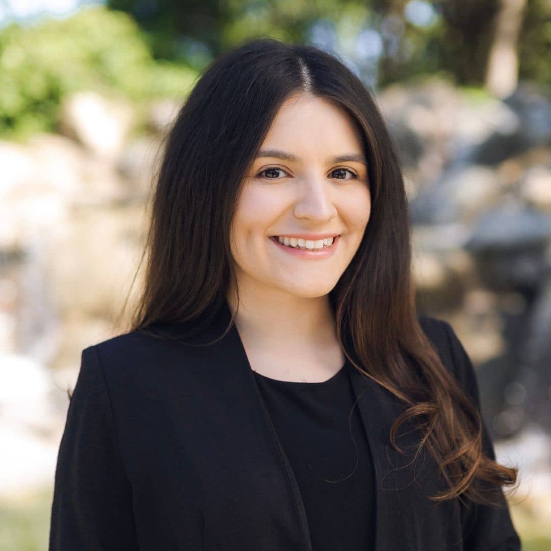 Smiling woman with long dark hair in a black blazer outdoors