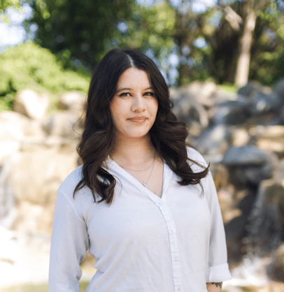 Zoe, in a white button-down shirt in front of a rock waterfall