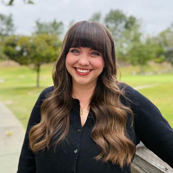 Smiling woman with long wavy hair in a black button-front sweater outdoors